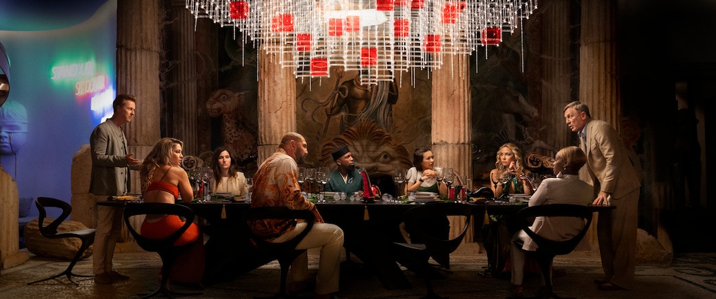 Photo from Glass Onion of guests sitting at a table while Daniel Craig yells at them
