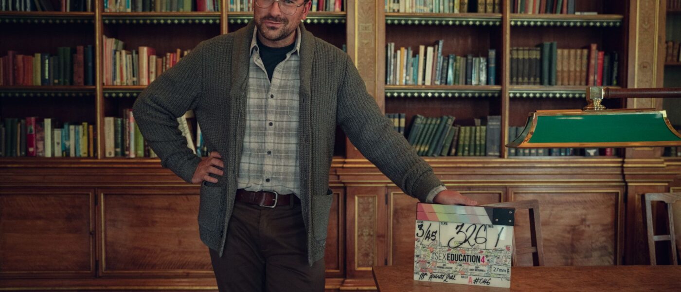 Photo of Dan Levy leaning on a desk from season 4 of Sex Education