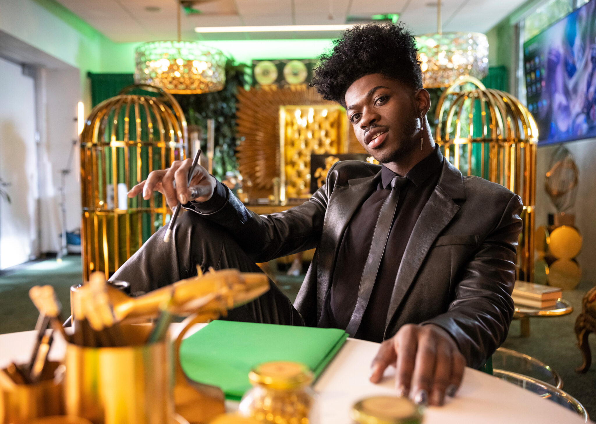 Photo of Lil Nas X sitting at a table in a fully black suit