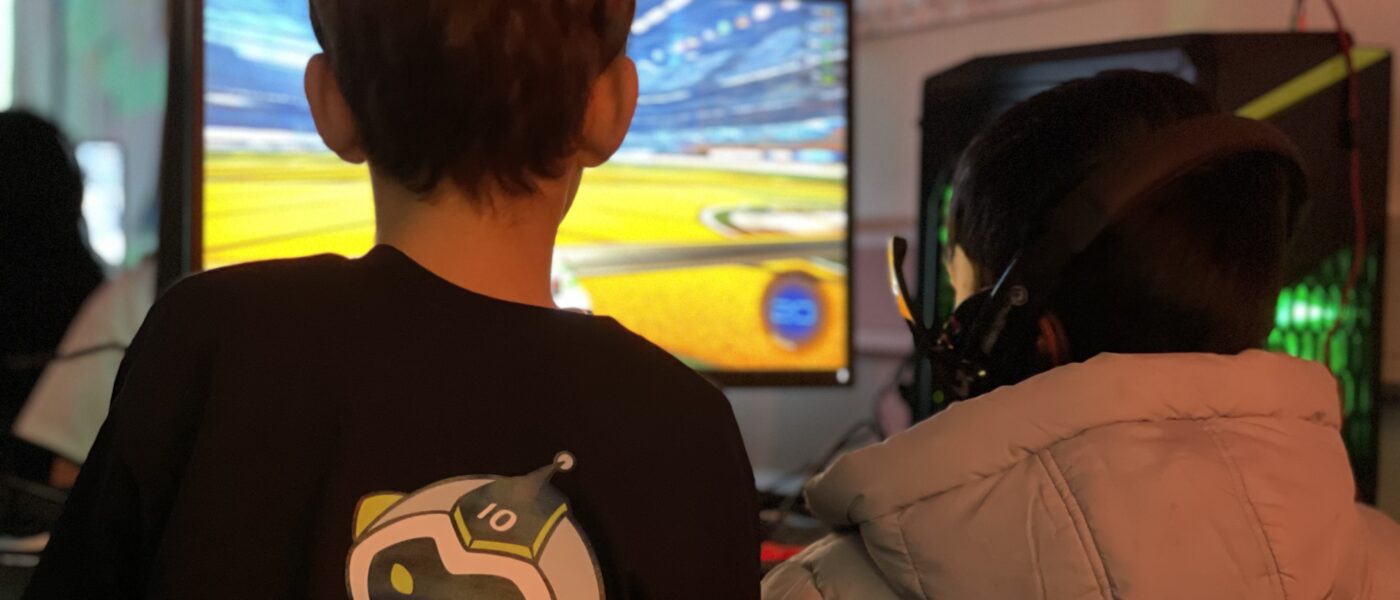 Kids playing games at a computer. One kid has a Tenstar logo on the back of their shirt