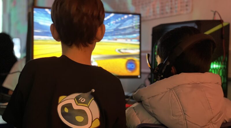 Kids playing games at a computer. One kid has a Tenstar logo on the back of their shirt