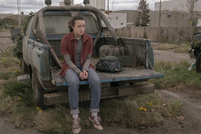 Bella Ramsey as Ellie in HBO's The Last of Us sitting on the bed of a dirty pickup truck