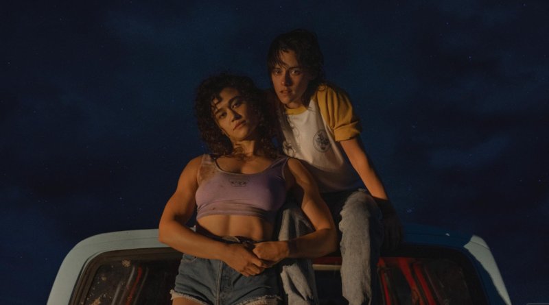Katy O'Brien (left) and Kristen Stewart (right) sitting on a car in promo photos for Love Lies Bleeding
